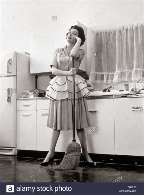 Download This Stock Image 1950s Woman Housewife Standing In Kitchen Leaning On Broom Br9e69