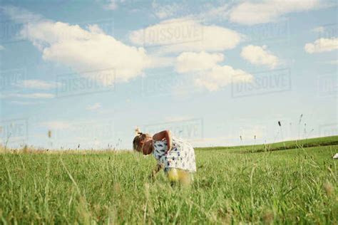 Female Toddler Bending Forward In Field Picking Grass Stock Photo