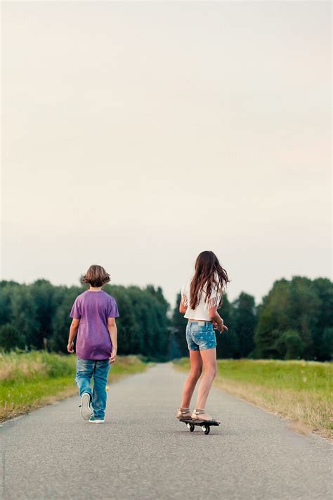Boy Walking Away And Girl On A Skateboard On A Long Path In The Fields