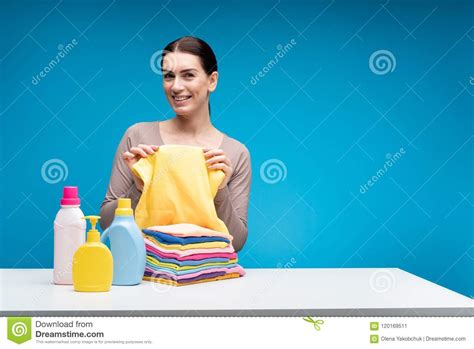 Mujer Alegre Que Muestra La Ropa Limpia En La Tabla Con Los Detergentes Imagen De Archivo