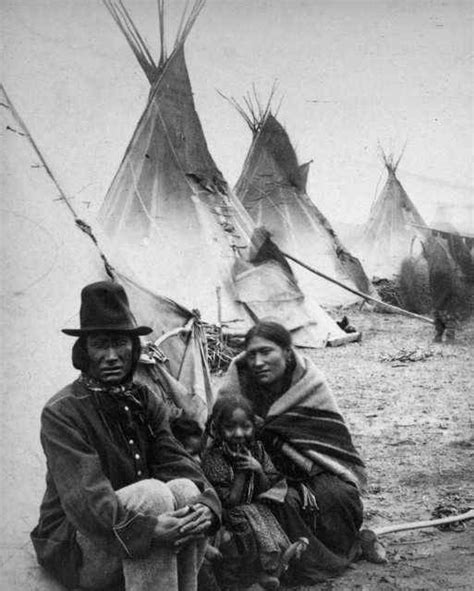 An Old Black And White Photo Of Two People Sitting In Front Of Teepees
