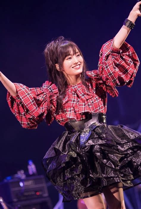 A Woman In A Red Plaid Shirt And Black Skirt On Stage With Her Arms Up