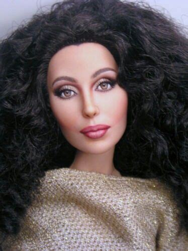 A Close Up Of A Doll With Long Black Hair Wearing A Gold Top And Silver
