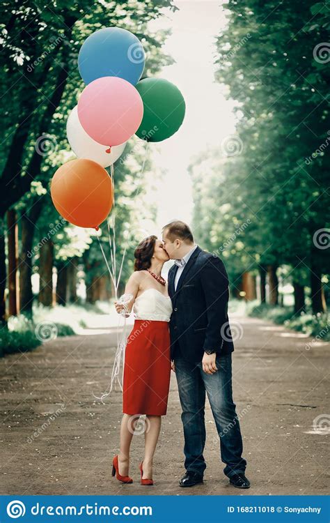 Fun Romantic Couple Kissing Outdoors Beautiful Woman Holding Balloons While Being Embraced By