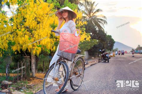 Slim Blonde Girl In Vietnamese White Long Dress And Hat Holds Bike With