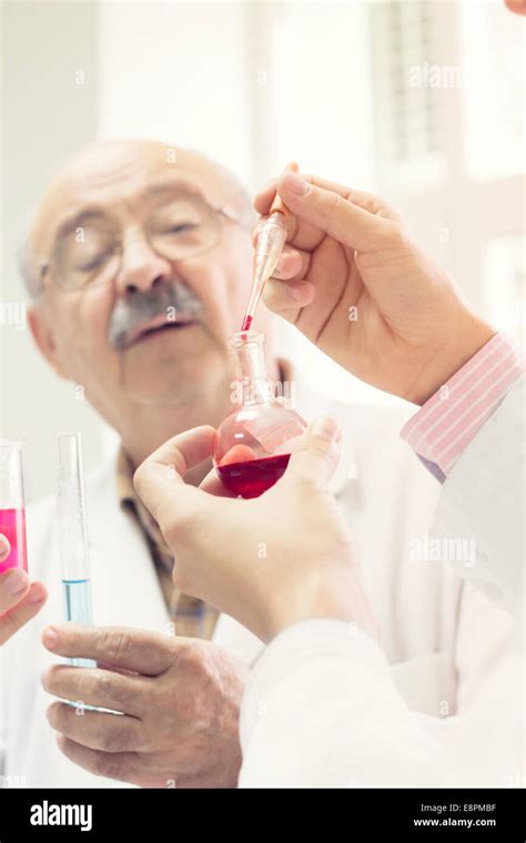 Scientist In A Laboratory Performing An Experiment With His Assistant Mixing Colorful Test