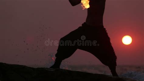 Man Turns Fire Poi Standing On A Cliff Near The Ocean At Sunset Stock