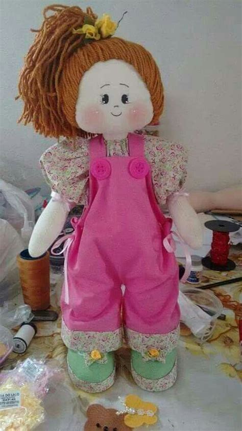 A Doll With Red Hair And Pink Overalls Sitting On A Table Next To