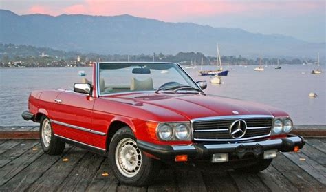 a red convertible car parked on top of a wooden dock next to the ocean