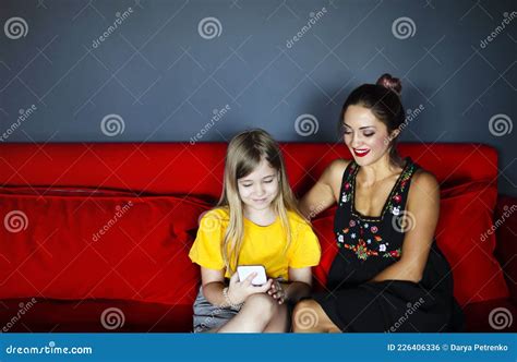 Happy Smiling Mother And Daughter Sitting On Sofa In Living Room While Using Smartphone Stock