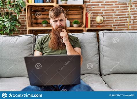 Redhead Man With Long Beard Using Laptop Sitting On The Sofa At The