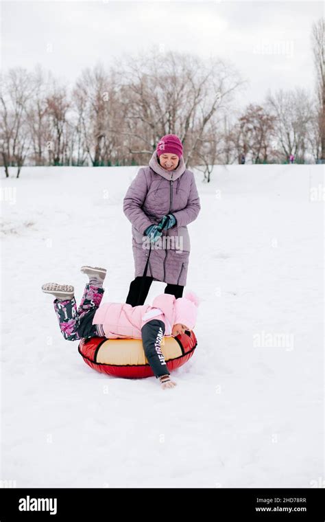 Distant Photo Of Kid On Sled With Grandmother Effortfully Pulling