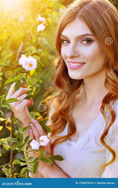 Portrait Of Beautiful Young Woman Posing By Rose Bush Stock Photo