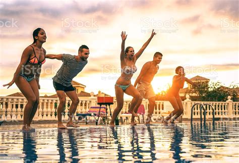 Group Of Happy Friends Jumping In The Pool At Sunset Young People 
