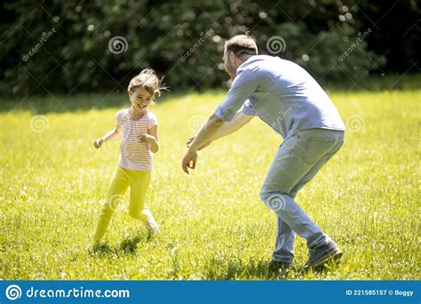 Father Chasing His Little Daughter While Playing In The Park Stock