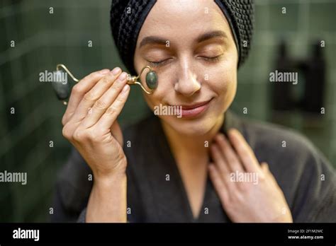 Woman Massaging Her Face With Roller In Robe With Hair Wrapped In A
