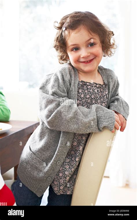 Portrait Of Smiling Little Girl Kneeling On A Chair At Home Stock Photo