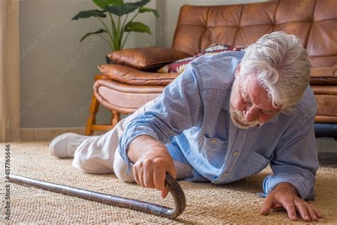 Elder Senior Man Lying On Floor After Falling Down With Wooden Walking Stick Beside Couch On Rug