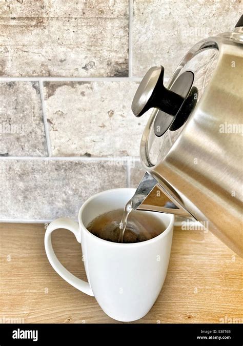 Pouring Hot Water Into A White Mug From The Kettle Making A Cup Of Tea In The Kitchen Stock