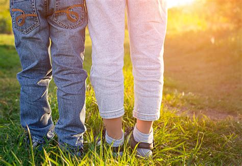 Two Pairs Of Childrens Legs In Jeans Outdoors In The Sun Stock Photo