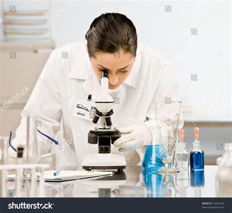 Curious Research Scientist In Lab Coat And Rubber Gloves Looking At