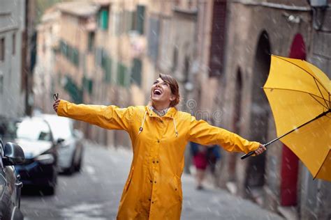A Young Girl With A Yellow Raincoat And Umbrella In A City Walk Is