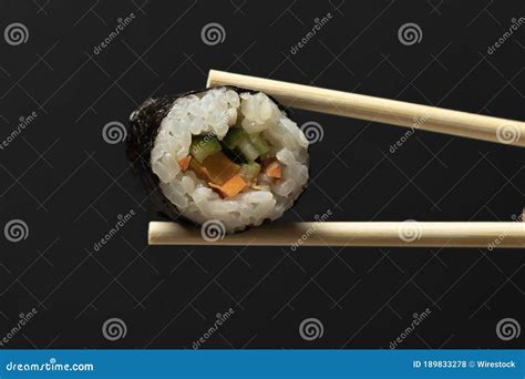 Horizontal Shot Of Two Chopsticks Holding A Single Sushi Roll Stock