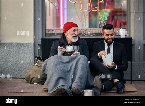 Smiling Rich And Poor Men Together Sitting On Street And Eat While