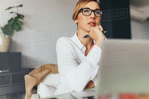 Pensive Looking Business Woman Sitting At Her Desk In Office Holding A Pen Woman Looking Away