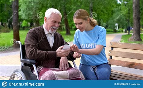 Female Volunteer Walking With Handicapped Patient In Hospital Park