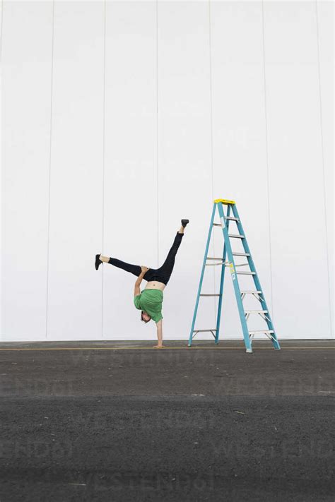 Acrobat Training One Armed Handstand Next To Ladder Stock Photo