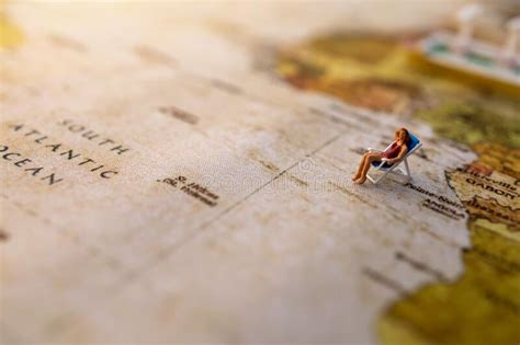 Miniature People Sit On Beach Sunbath Seats On Vintage World Map