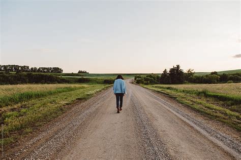Woman Walking On Road Through Beautiful Countryside At Dusk By