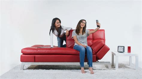 Two Women Sitting On A Red Couch And One Is Holding A Cell Phone