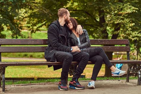 Attractive Modern Couple Sitting On A Bench In A Park Stock Photo