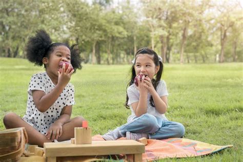 Happy Cheerful Ethnic Girls Eat Apple Together At Outdoors Park