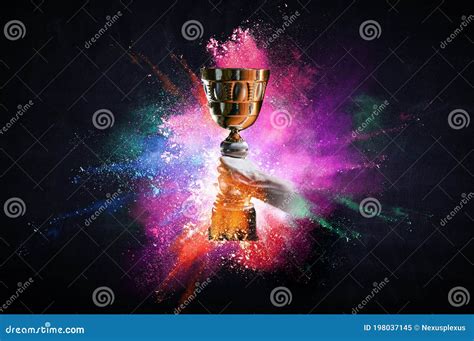 Hand Holding Up A Gold Trophy Cup Against Dark Background Stock Image