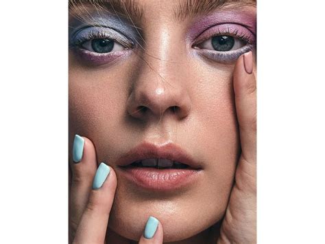 A Woman With Blue And Pink Makeup Holding Her Hands To Her Face While Looking At The Camera