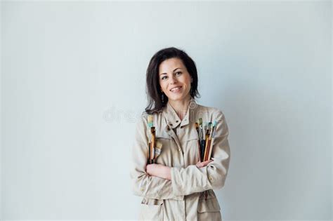 A Woman Artist Stands With Brushes To Paint Against A White Wall Stock