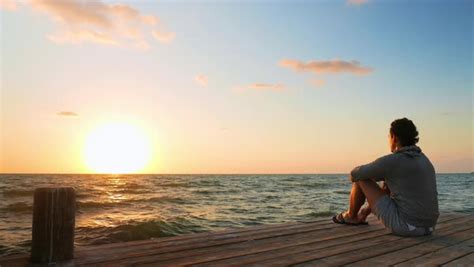 Man Sitting On Pier Watching Sunset Over Ocean Stock Video Footage