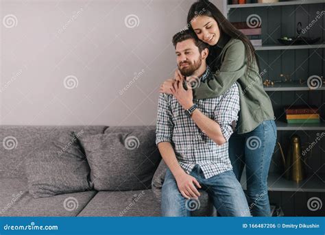 Young Happy Couple Is Embracing In Cozy Living Room Girl Hugging Her