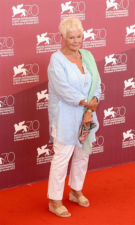 An Older Woman Standing In Front Of A Red Wall Wearing White Pants And