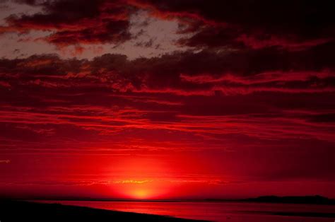The Sun Is Setting Over An Ocean With Red Clouds