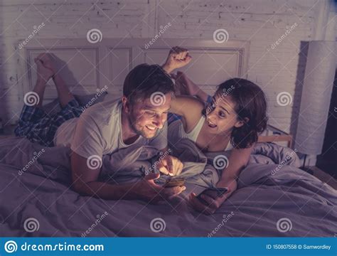 Couple On Mobile Phones In Bed Late At Night Enjoying Social Network Games And Internet