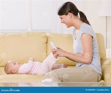 Mother Putting Shoes On Baby On Sofa At Home Royalty Free Stock Photos