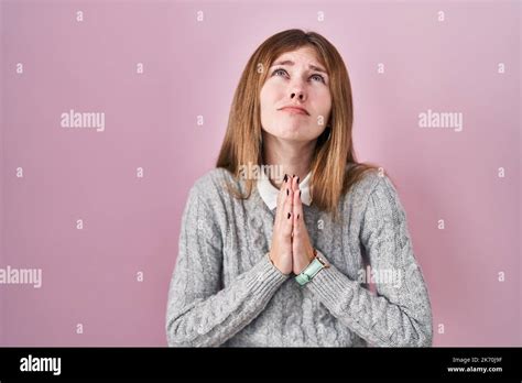beautiful woman standing over pink background begging and praying with hands together with hope