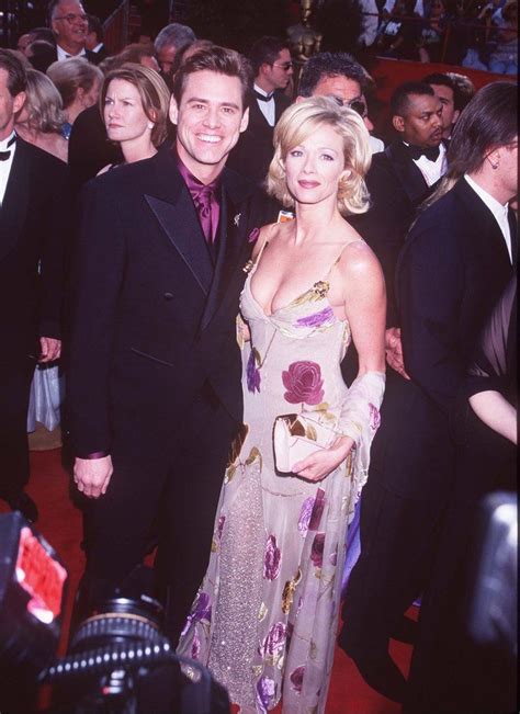A Man And Woman Standing Next To Each Other On A Red Carpet At An Event