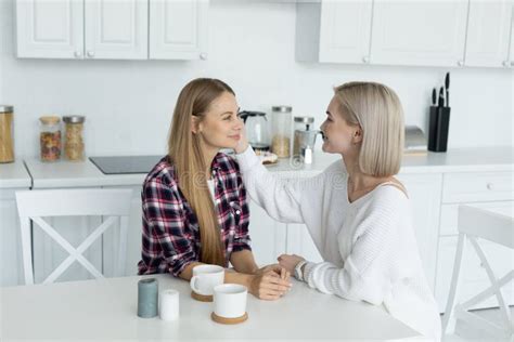 Two Attractive Lesbian Female In Casual Clothes Sitting Together At The Table In The Kitchen
