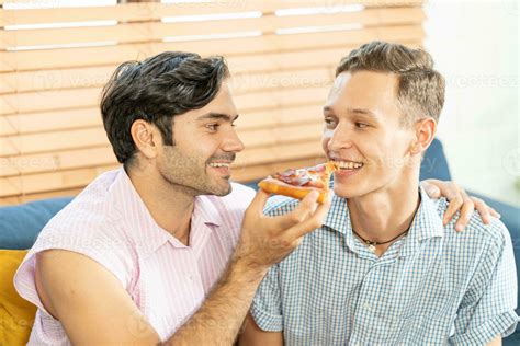 Cheerful Gay Couple Eating Pizza Gay Couple Sitting On Sofa At Home Eating One Slice Of Pizza