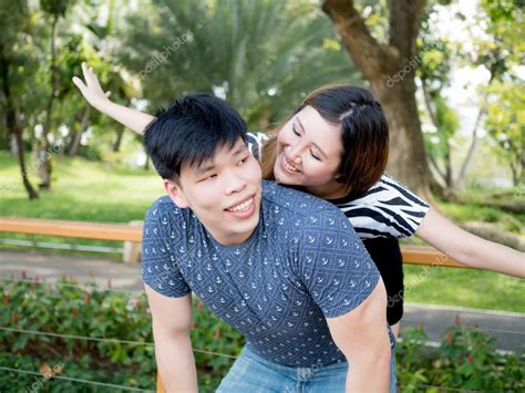 Young Asian Couple Having Piggy Back Together In Green Nature